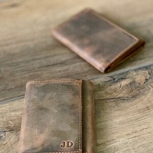 May include: Two brown leather wallets, one folded open to reveal the initials "JD" embossed on the inside.