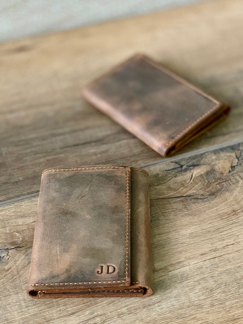 May include: Two brown leather wallets, one folded open to reveal the initials "JD" embossed on the inside.
