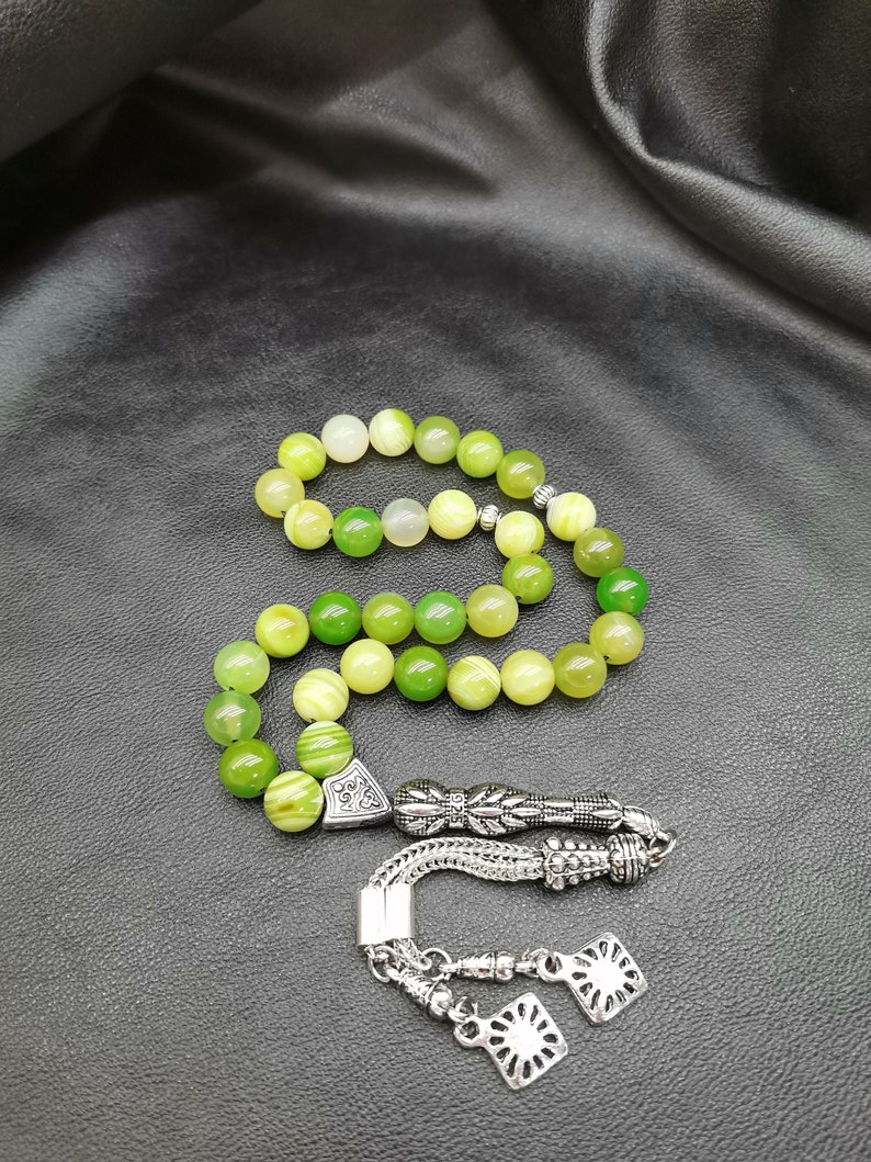Pu&ograve; includere: Una collana di grani di preghiera verdi e gialli con elementi metallici argentati ornati. Le perle sono rotonde e variano nelle tonalit&agrave; di verde e giallo. La metalleria include motivi decorativi e un nappa.