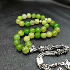 Pu&ograve; includere: Un rosario di preghiera con perline verdi con nappa e decorazioni argentate. Le perline variano in tonalit&agrave; di verde e giallo. La nappa e gli elementi decorativi sono in metallo argentato.