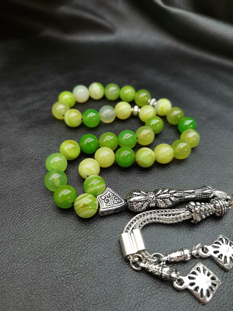 Pu&ograve; includere: Un rosario di preghiera con perline verdi con nappa e decorazioni argentate. Le perline variano in tonalit&agrave; di verde e giallo. La nappa e gli elementi decorativi sono in metallo argentato.