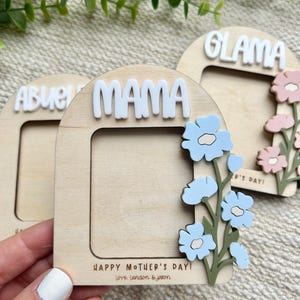 May include: Wooden Mother's Day photo frames with the words "MAMA" and "GLAMA" in white. The frames are decorated with blue and pink flowers. The phrase "HAPPY MOTHER'S DAY! Love. Landon & Jaxon" is printed on the frame.
