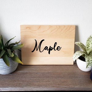 May include: A wooden cutting board with the word "Maple" written in black cursive lettering.