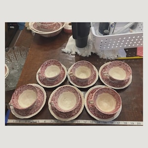May include: A set of five teacups and saucers featuring a red and white floral pattern. The cups and saucers are arranged on a wooden surface next to a measuring tape that shows a length of 20 inches across the bottom of the display.