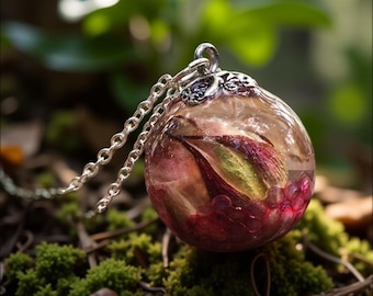 May include: A spherical clear resin pendant necklace featuring an encased dried rosebud with green and pink petals, accented by small red beads at the base. The pendant is attached to a silver-toned metal chain with a decorative filigree bail.