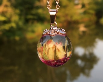 May include: A gold chain necklace with a clear glass pendant containing a dried rose and pink beads.