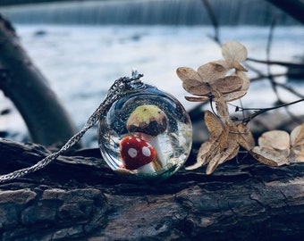 May include: A silver chain necklace with a clear glass pendant containing a miniature red and white mushroom and a yellow mushroom.