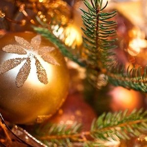 May include: A gold Christmas ornament with a white snowflake design, surrounded by pine branches and other ornaments.