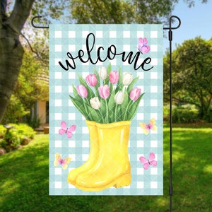 May include: A garden flag with a blue and white checkered background. The flag features the word "welcome" in black script above a yellow rain boot filled with pink and white tulips. Pink and yellow butterflies are scattered around the design.