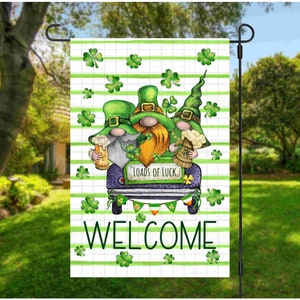 Può includere: Una bandiera da giardino di benvenuto verde, bianca e nera con tre folletti che viaggiano in auto. L'auto ha la scritta "Loads of Luck" sul lato. La bandiera ha un motivo a trifoglio verde e la parola "WELCOME" in grandi lettere.