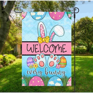 Pode incluir: Uma bandeira de jardim de boas-vindas rosa e azul com um design de coelho. A bandeira diz "Bem-vindo a todos os coelhos" e apresenta ovos de Páscoa coloridos.