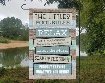 May include: A wooden sign with blue and green stripes that reads "The Littles Pool Rules" with the following rules: Relax, Swim at your own risk! Lifeguard is playing Cornhole!, Enjoy the Music, Soak up the Sun, Proudly Serving Whatever You Bring!