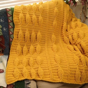 May include: A crocheted throw blanket in a mustard yellow color with a leaf pattern.
