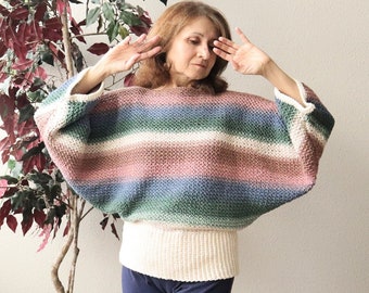 May include: A striped, multi-colored crochet sweater with long sleeves and a loose fit. The sweater is made with a variety of shades of pink, blue, green, and white yarn.
