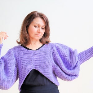 May include: A purple crocheted sweater with a cropped length and large, puffy sleeves.