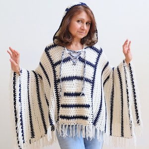 May include: A white and navy blue striped crochet poncho with a hood and fringe. The poncho has a lace-up detail at the neck.