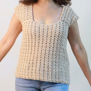 May include: A beige crochet top with a scoop neck and short sleeves. The top has a delicate openwork pattern.
