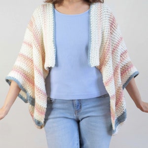 Könnte beinhalten: Eine gestrickte gestreifte Strickjacke in Weiß-, Rosa- und Blautönen. Die Strickjacke hat eine lockere Passform und einen weiten, offenen Ausschnitt.