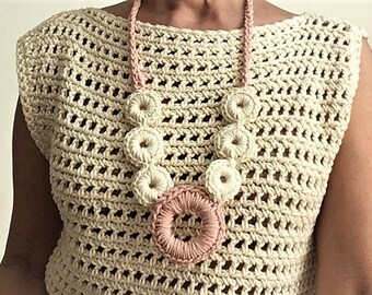 Puede incluir: Un top de crochet con un delicado patrón de calado en color crema. El top presenta un collar llamativo con grandes flores de crochet en tonos crema y rosa.