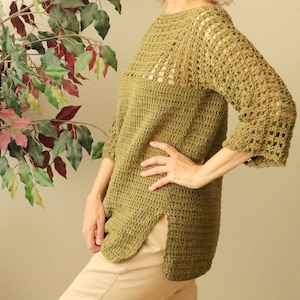 May include: A green crochet top with a lacy design on the sleeves and neckline. The top has a relaxed fit and a slightly longer length in the back.