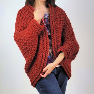 May include: A red crocheted cardigan with a loose fit and long sleeves. The cardigan is open in the front and has a simple design.