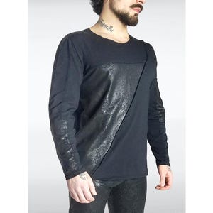May include: Black long-sleeve shirt with a diagonal textured panel across the front. The sleeves have a textured design. The shirt is made of a soft, comfortable material.