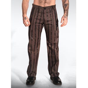 Könnte beinhalten: Braune Hose mit vertikalem schwarzen Streifenmuster. Die Hose verfügt über einen Standardbund mit einem einzelnen Knopfverschluss, einen Reißverschluss vorne und einen geradlinigen Schnitt. Der Stoff hat einen durchgehend dunkelbraunen Farbton.