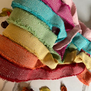 May include: A collection of colorful fabric ribbon trim with a diamond pattern. The ribbon is frayed on the edges and has a textured woven look.