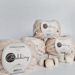May include: Three balls of beige cotton candy yarn, each labeled "Cotton Candy" and "Bobbiny" with the weight of 150 grams. The yarn is 100% recycled cotton.