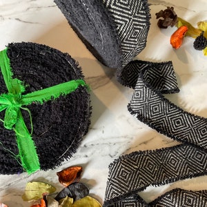 May include: Two black and white patterned fabric trims with frayed edges. One trim is rolled up and the other is laying flat. The trim has a geometric diamond pattern.