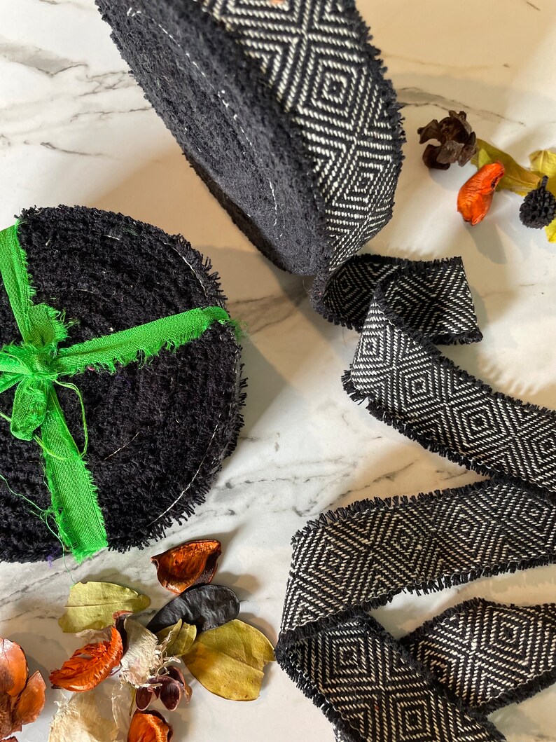 May include: Two black and white patterned fabric trims with frayed edges. One trim is rolled up and the other is laying flat. The trim has a geometric diamond pattern.