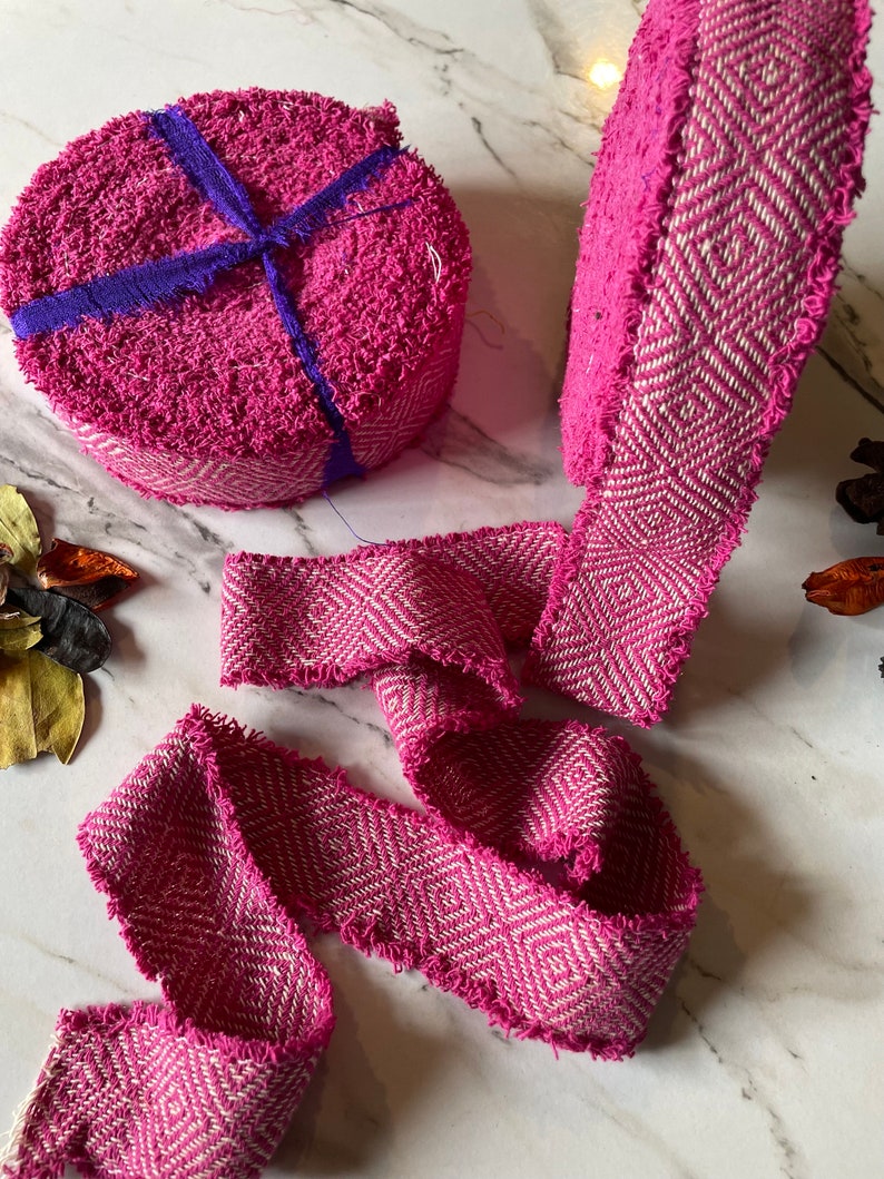 May include: Pink and white woven ribbon with a chevron pattern. The ribbon is frayed on the edges and is rolled up into two coils.