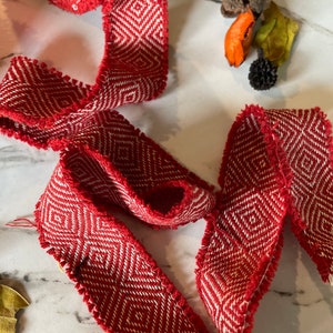 May include: Red and white woven ribbon with a geometric pattern. The ribbon has a frayed edge.