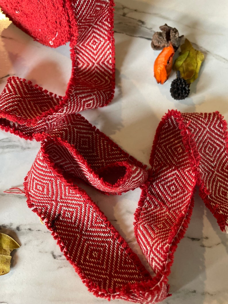 May include: Red and white woven ribbon with a geometric pattern. The ribbon has a frayed edge.