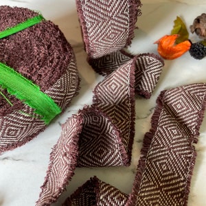 May include: Brown and white woven ribbon with a diamond pattern and frayed edges. The ribbon is rolled up and laid out flat.