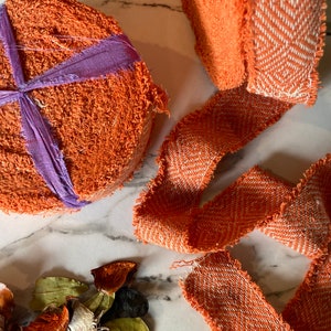 May include: Two orange fabric rolls with a white and orange patterned trim. The rolls are on a white marble surface with dried flower petals.