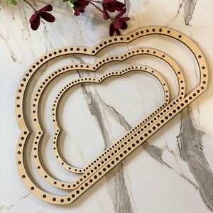 May include: Three wooden knitting looms in the shape of a cloud, stacked on top of each other. The looms are made of natural wood and have a light brown color.