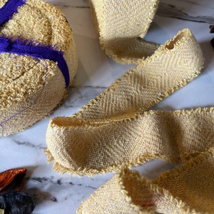 May include: A close-up of a yellow and white woven ribbon with a frayed edge. The ribbon is folded and arranged on a white marble surface.