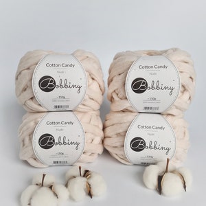 May include: Four balls of nude colored cotton candy yarn, each weighing 150 grams. The yarn is made of 100% recycled cotton. The yarn is labeled "Cotton Candy" and "Bobbiny".