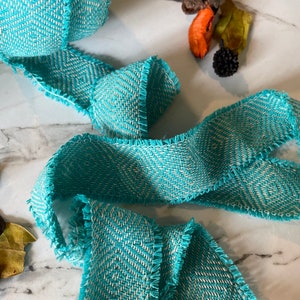 May include: Teal and white chevron patterned ribbon with frayed edges. The ribbon is woven and has a textured surface.