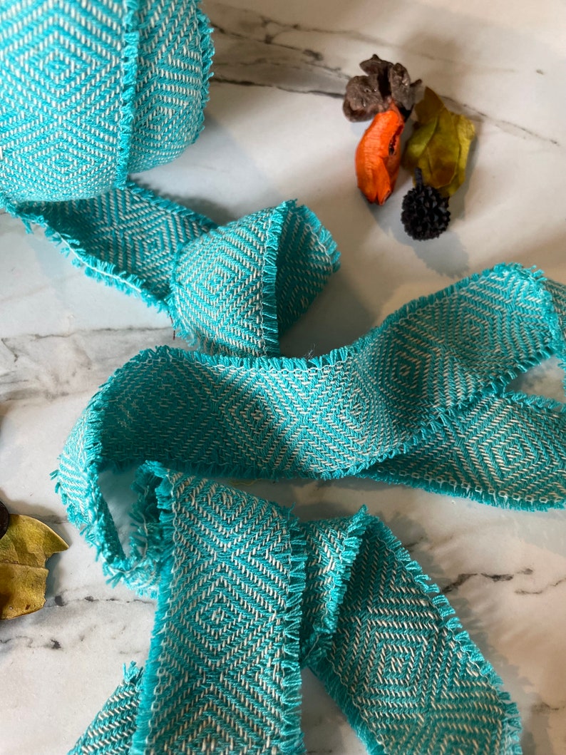 May include: Teal and white chevron patterned ribbon with frayed edges. The ribbon is woven and has a textured surface.