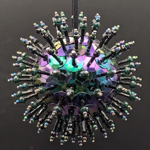 May include: A spherical ornament with iridescent sequins and beaded spikes. The ornament has a black hanging string. The sequins shift in color from purple to green. The spikes are made of black beads and green accents.