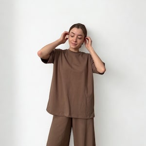 May include: A brown, oversized t-shirt and matching wide-leg trousers set. The short-sleeved top has a relaxed fit, and the trousers have a high waist. The outfit is made of a soft, solid-coloured fabric, suitable for casual wear.