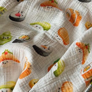 May include: White fabric with a repeating pattern of various sushi pieces, including nigiri and rolls. The sushi illustrations have smiling faces and are in shades of orange, green, and black. The fabric has a crinkled texture.