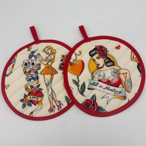 May include: Two round, quilted pot holders with red trim and hanging loops. Each features a pin-up girl design with tattoo-style art. One says "Don't Gamble With Love," the other says "All or Nothing."