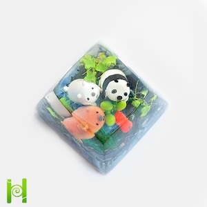 May include: A clear resin keycap with a panda bear, a polar bear, and a brown bear figurine inside. The bears are surrounded by green and blue resin, resembling a forest scene.