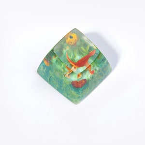 May include: A clear green and yellow resin cube with a red and yellow fish design inside.