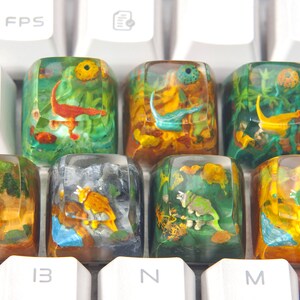 May include: Eight colorful keycaps with dinosaur and prehistoric animal illustrations encased in clear resin. The keycaps are arranged in two rows of four on a white keyboard.