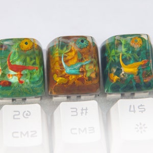 May include: Three resin keycaps with colorful underwater scenes. The keycaps are green, brown, and blue with yellow, orange, and red accents. The keycaps are labeled with the numbers 2, 3, and 4.