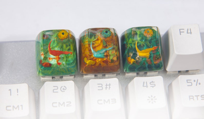 May include: Three resin keycaps with colorful underwater scenes. The keycaps are green, brown, and blue with yellow, orange, and red accents. The keycaps are labeled with the numbers 2, 3, and 4.